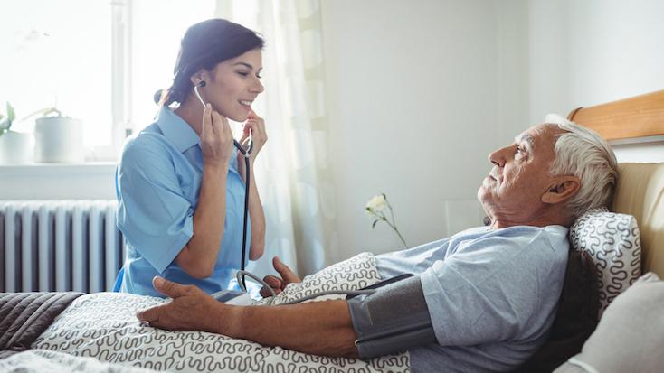 nurse checking an elderly man's blood pressure in bed